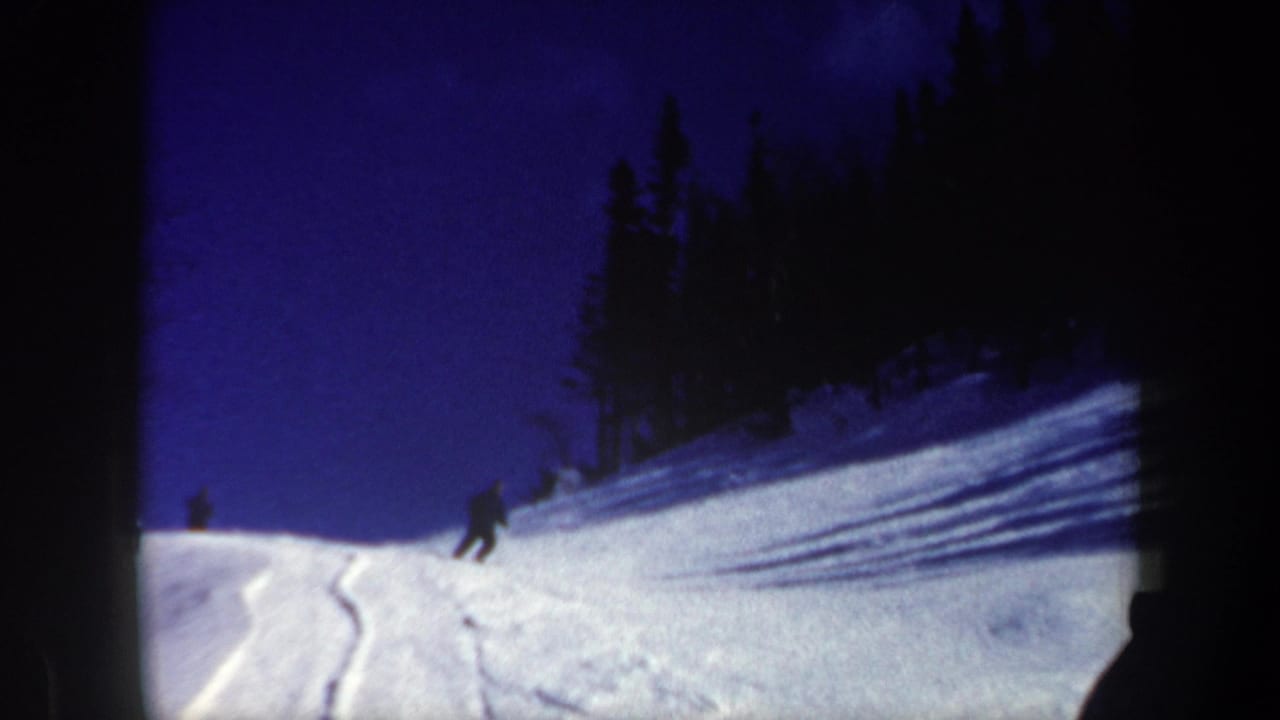 1962 New Hampshire frame of a skier descending a powdery slope with forest shadows and a deep blue winter sky.