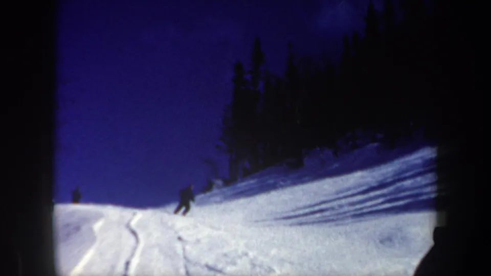 1962 New Hampshire frame of a skier descending a powdery slope with forest shadows and a deep blue winter sky.