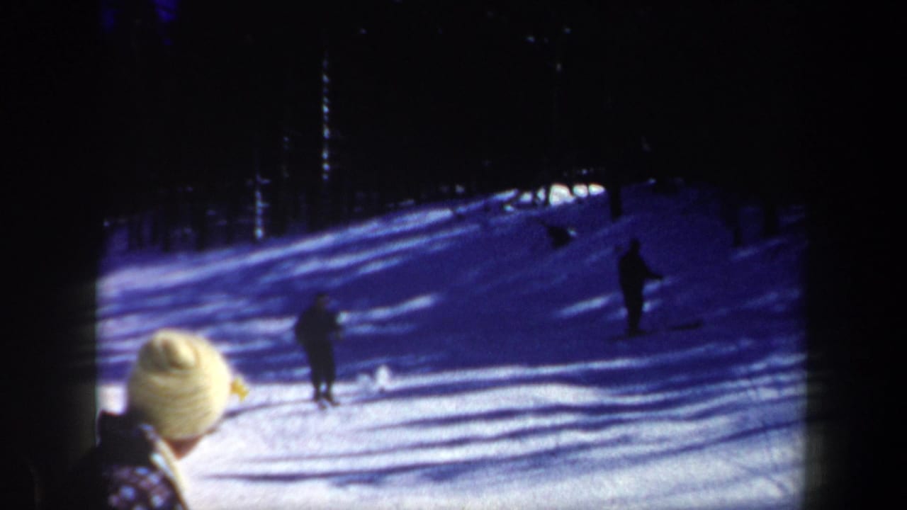 1962 New Hampshire 8mm frame showing a skier on a snowy slope with dark trees and a bundled spectator in the foreground.