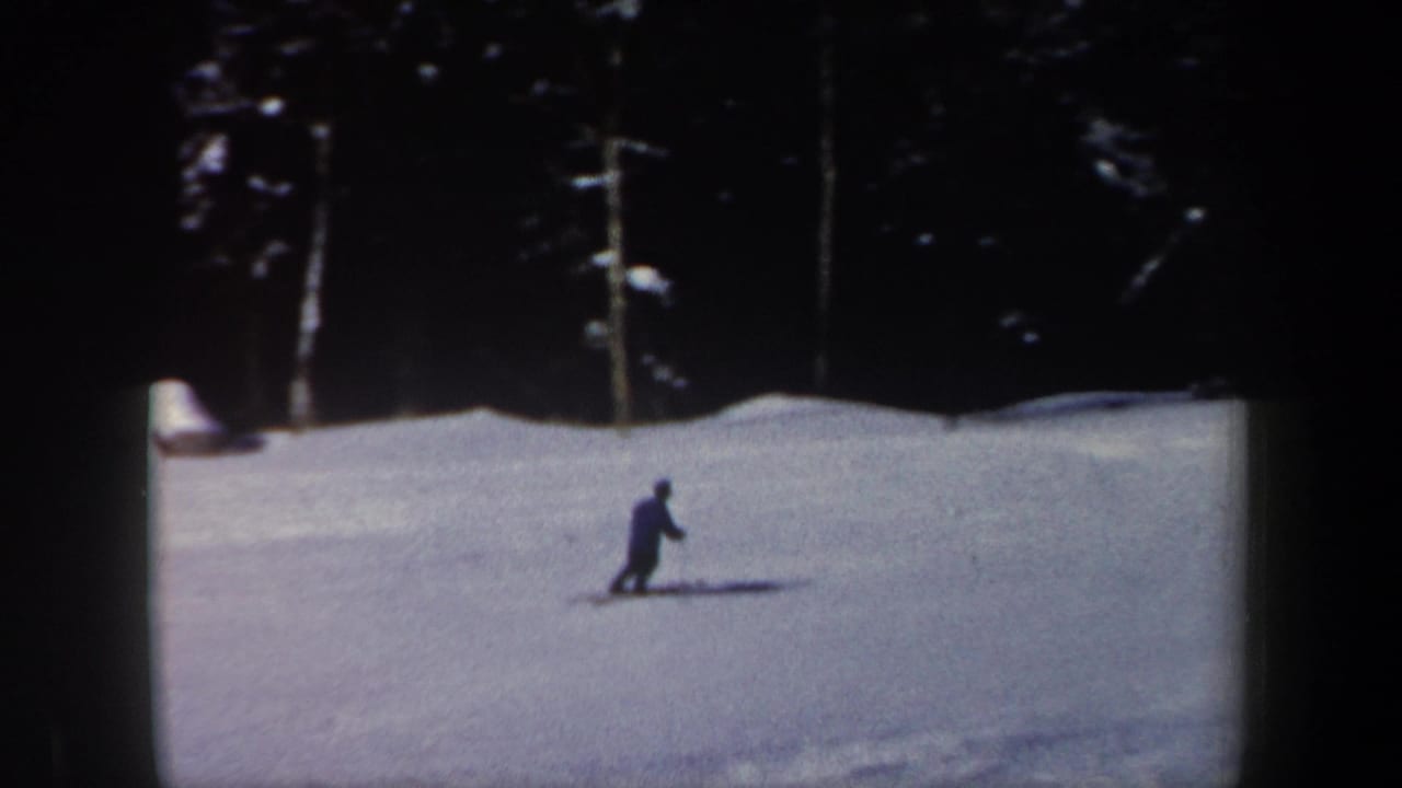 1962 New Hampshire 8mm frame showing a skier moving across an open slope bordered by dark evergreens and strong winter shadows.