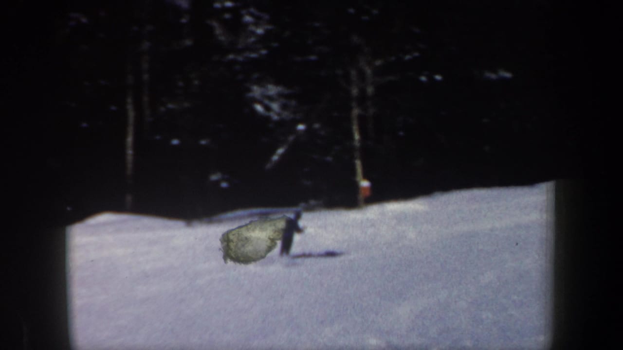 1962 New Hampshire 8mm frame showing a distant skier crossing a snow-covered slope near a dark tree line.