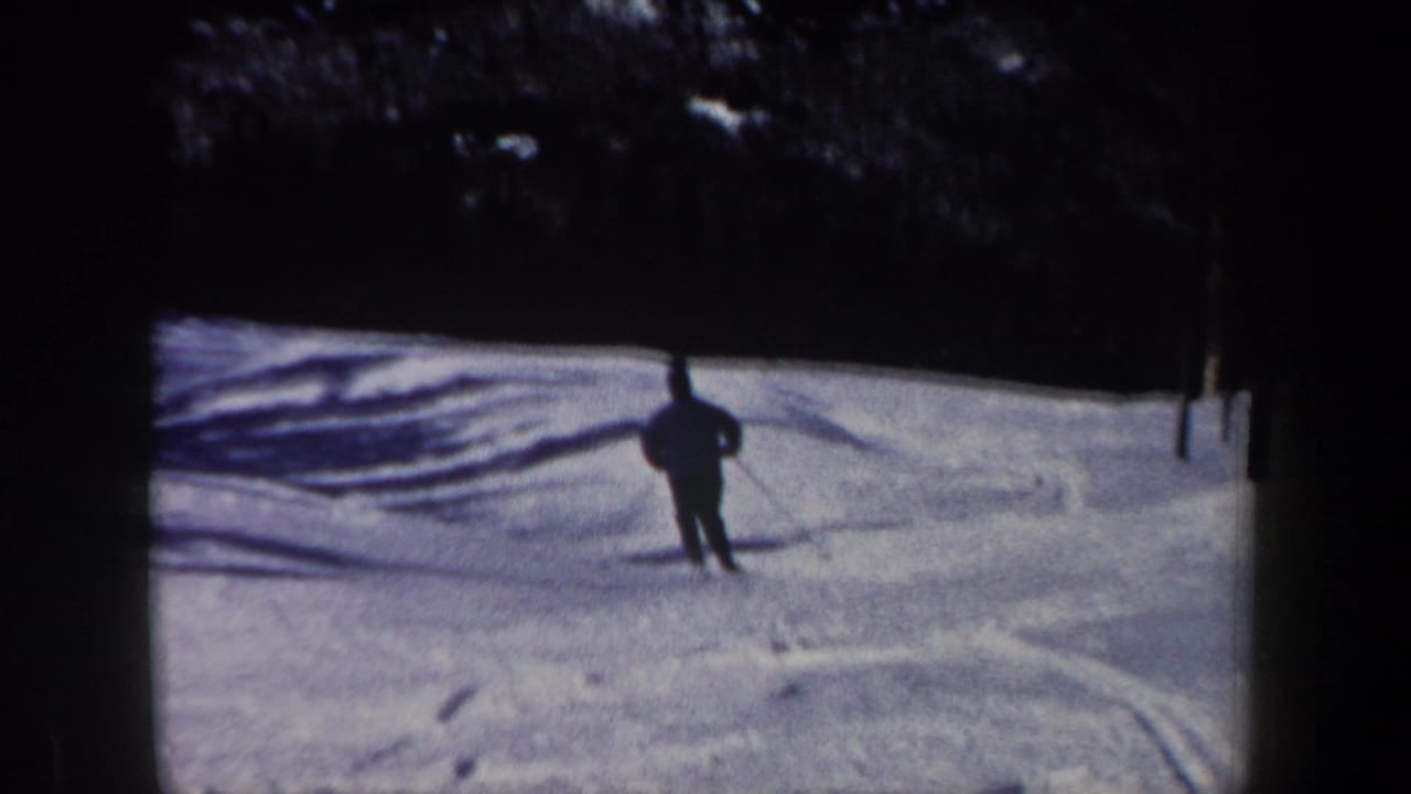 1962 New Hampshire 8mm frame showing a skier from behind on a snow-covered run marked by tracks and shadows.