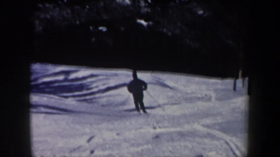 1962 New Hampshire 8mm frame showing a skier from behind on a snow-covered run marked by tracks and shadows.