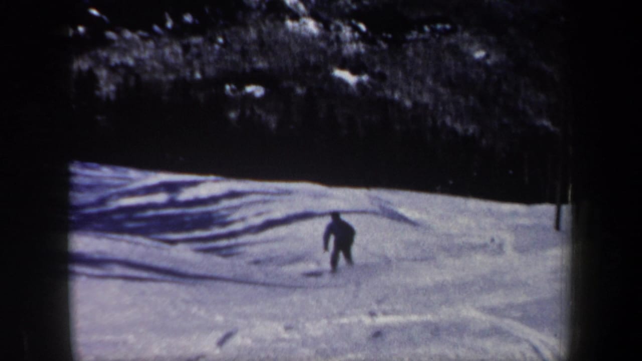 Lone skier descends a snowy slope beneath a dark treeline.