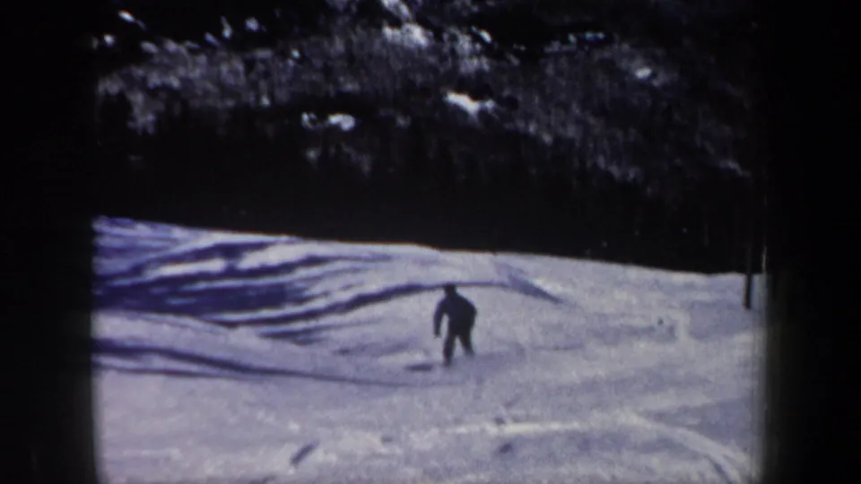 A distant skier in dark winter clothing moves down a snowy New Hampshire slope in 1962 home-movie footage.