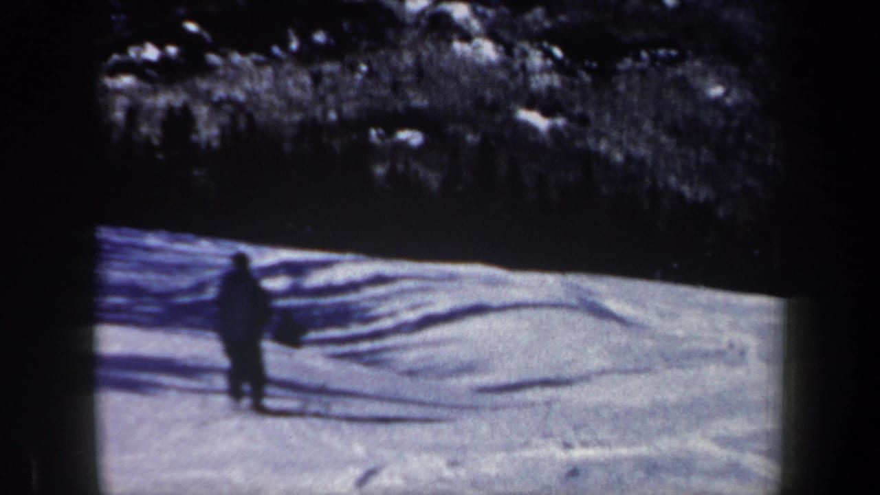 Distant skier stands or slows on the snowy slope near shadowed snow.