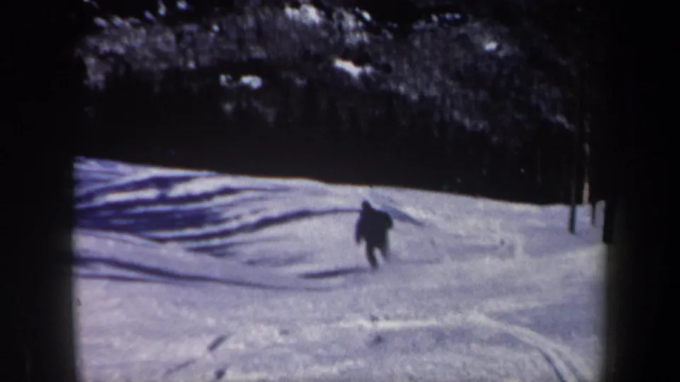 A dark-clad skier continues downhill on a snowy New Hampshire slope in grainy 1962 8mm footage.