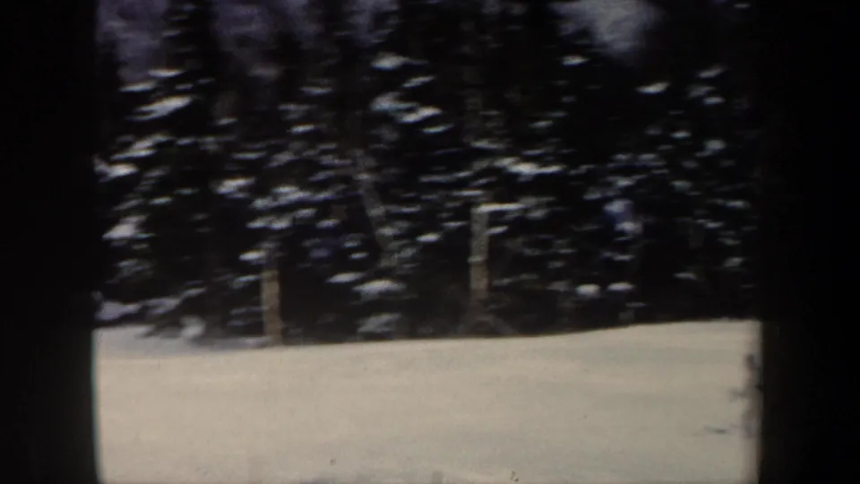 1962 New Hampshire 8mm frame with a snowfield, dark evergreen woods, and a partially visible skier at the edge of the shot.