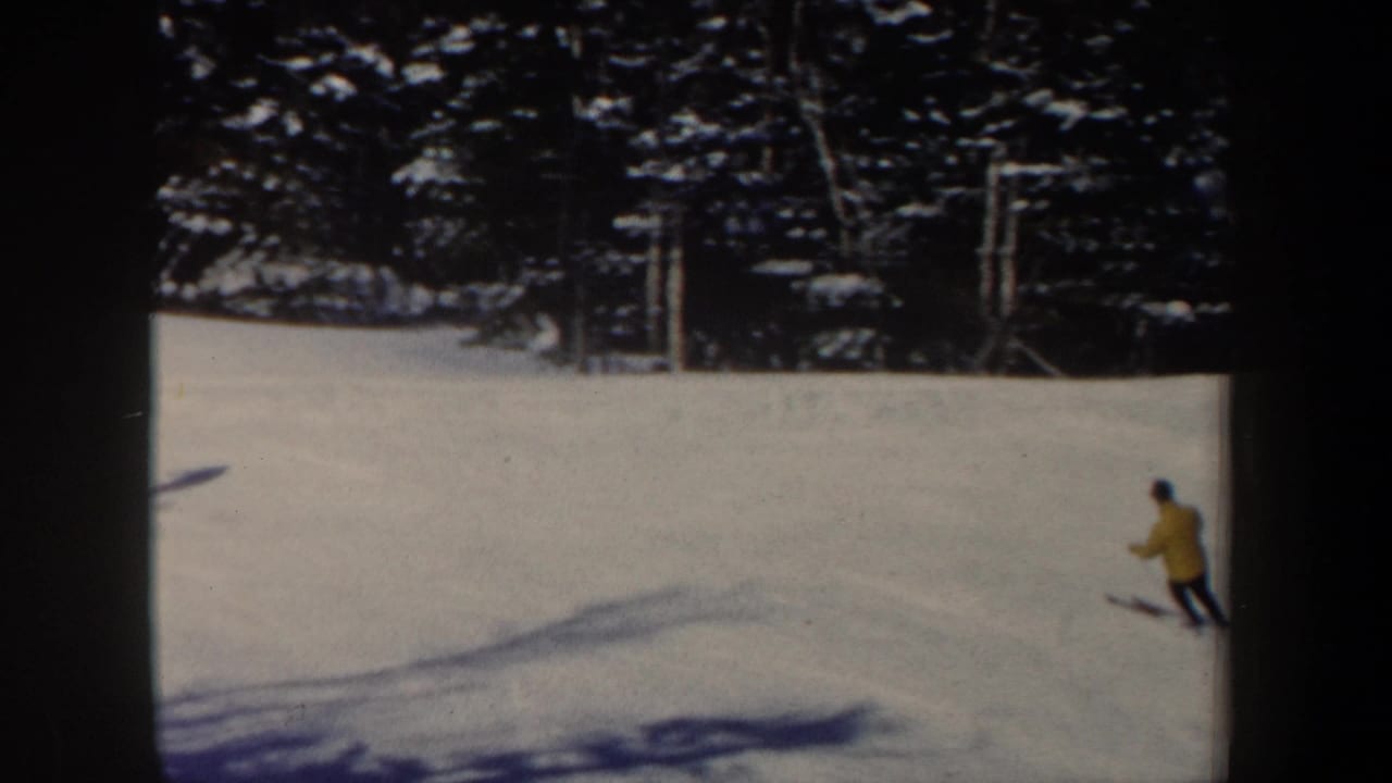 1962 New Hampshire 8mm frame showing a distant skier in a yellow jacket moving across a snowy wooded slope.