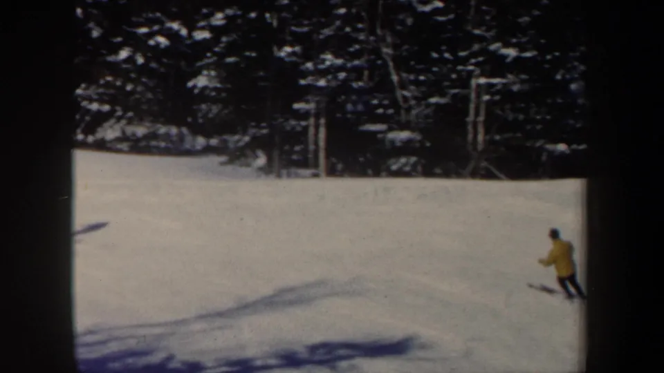 1962 New Hampshire 8mm frame showing a distant skier in a yellow jacket moving across a snowy wooded slope.