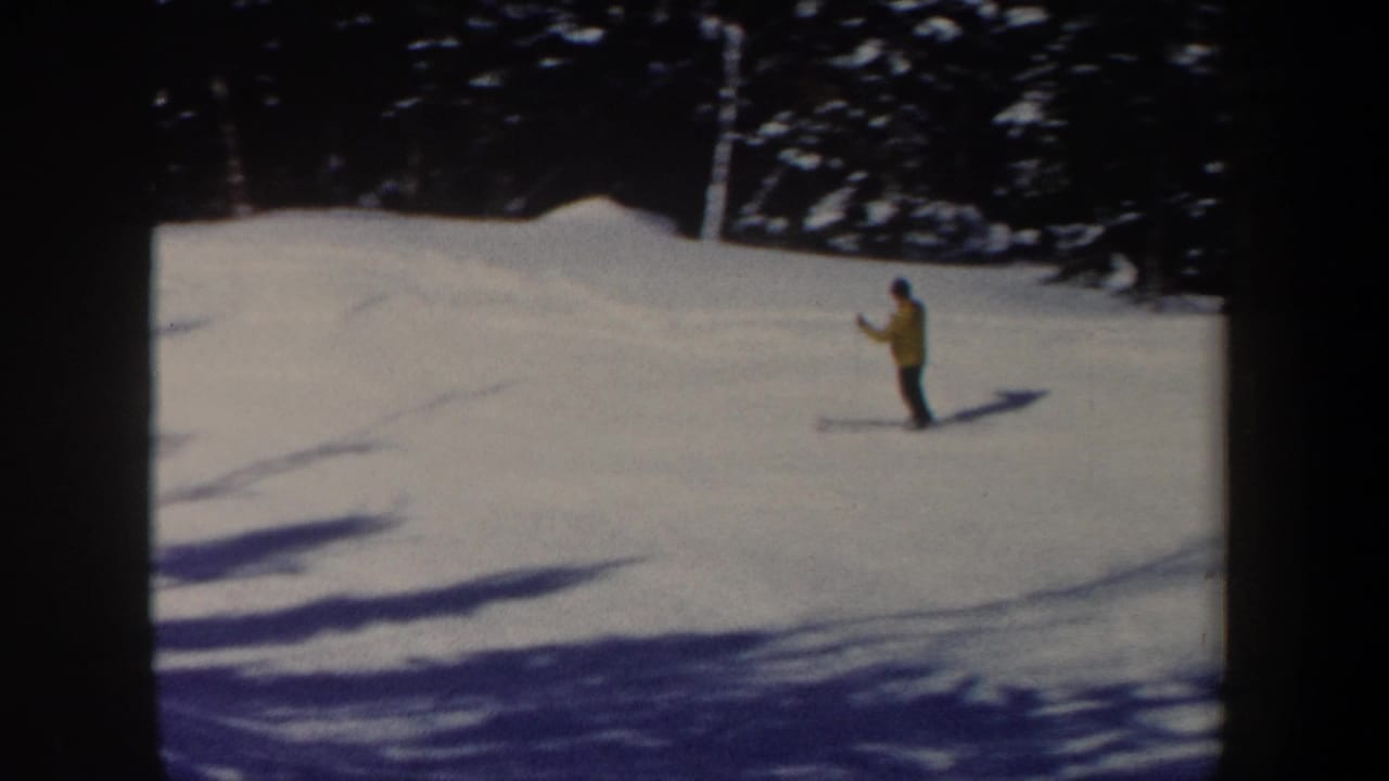 1962 New Hampshire home-movie frame with a yellow-jacketed skier on open snow below a wooded edge.