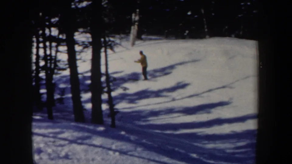 1962 New Hampshire 8mm still showing a yellow-jacketed skier near tall trees and shadowed snow.