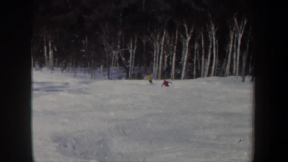 1962 New Hampshire 8mm frame showing two distant skiers on a white slope bordered by leafless woodland.