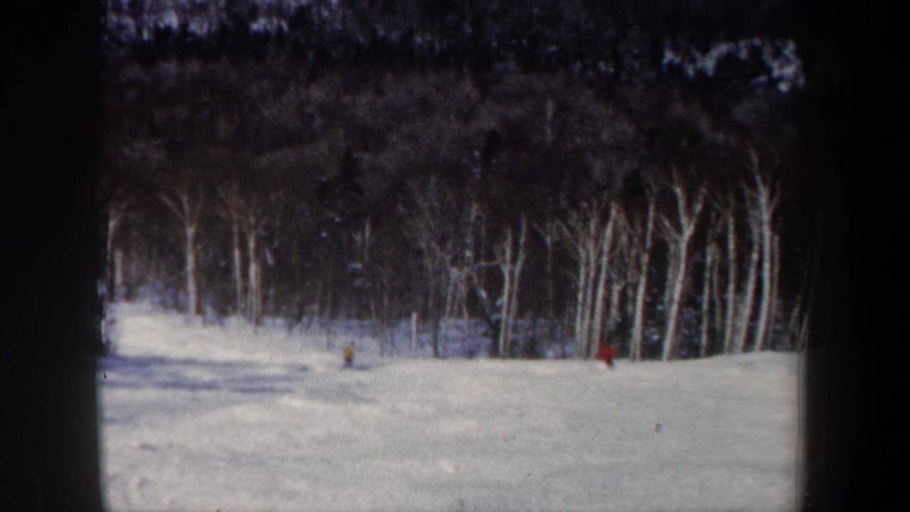 1962 New Hampshire 8mm frame showing distant skiers on a snow-covered slope at the edge of a leafless forest.