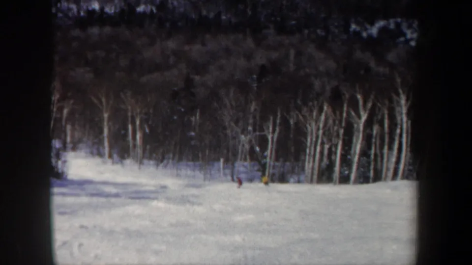 Distant skiers in colored winter clothing cross a snowy New Hampshire slope in this 1962 home-movie frame.