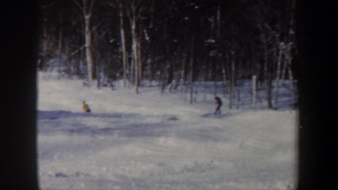 Distant skiers in bright jackets move across a snowy wooded slope in 1962 New Hampshire home-movie footage.