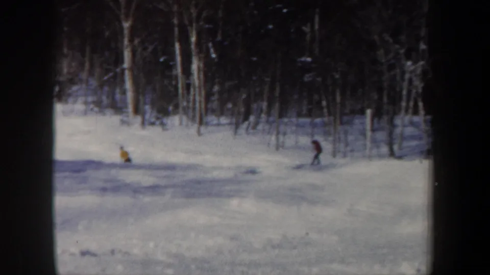 Distant skiers in bright jackets move across a snowy wooded slope in 1962 New Hampshire home-movie footage.