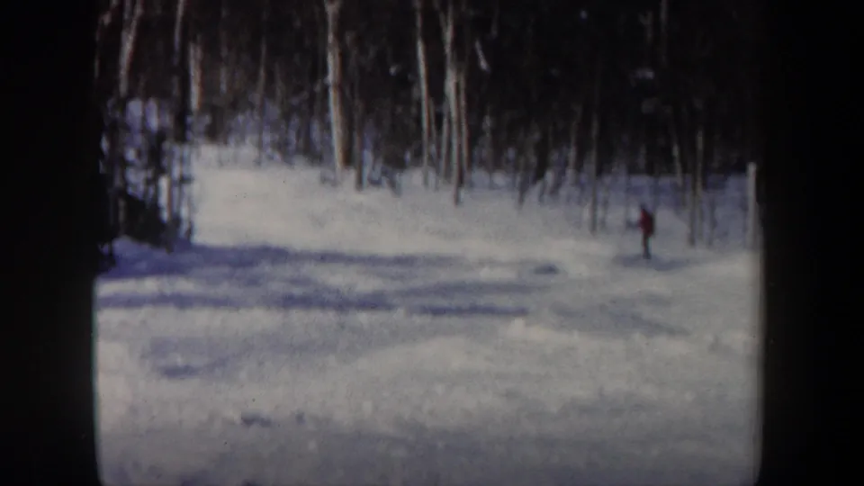A distant skier glides along a snowy tree-lined slope in 1962 New Hampshire 8mm footage.