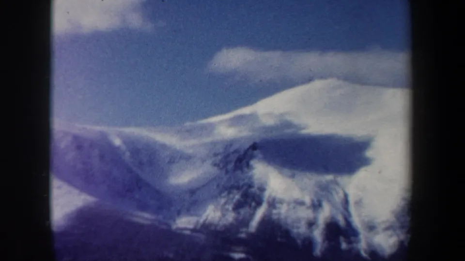 1962 New Hampshire 8mm frame of a rounded snowy peak, cloud bands, blue sky, and dark forested foreground.