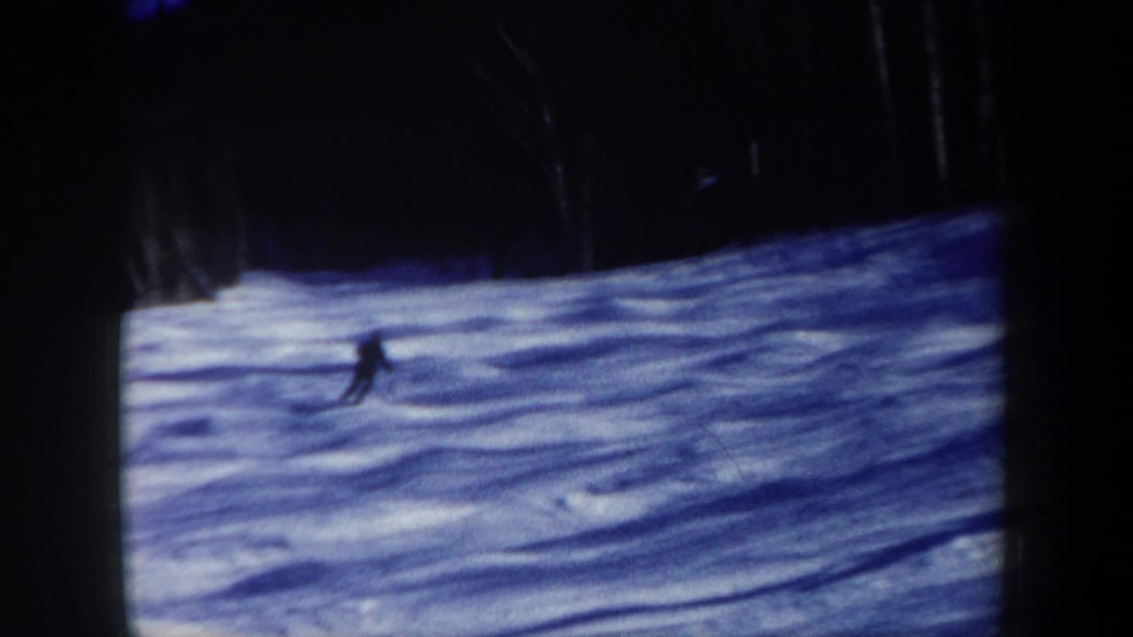 1962 New Hampshire 8mm frame showing a lone skier in dark clothing crossing a snowy slope near a forest edge.