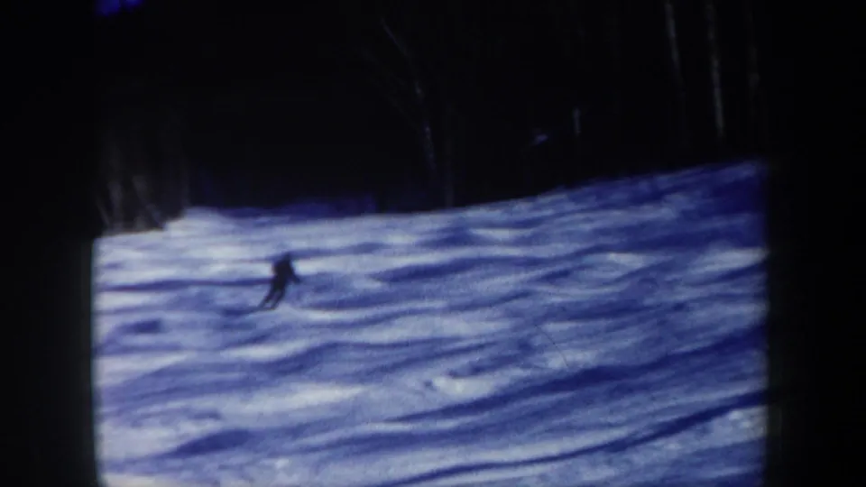 1962 New Hampshire 8mm frame showing a lone skier in dark clothing crossing a snowy slope near a forest edge.