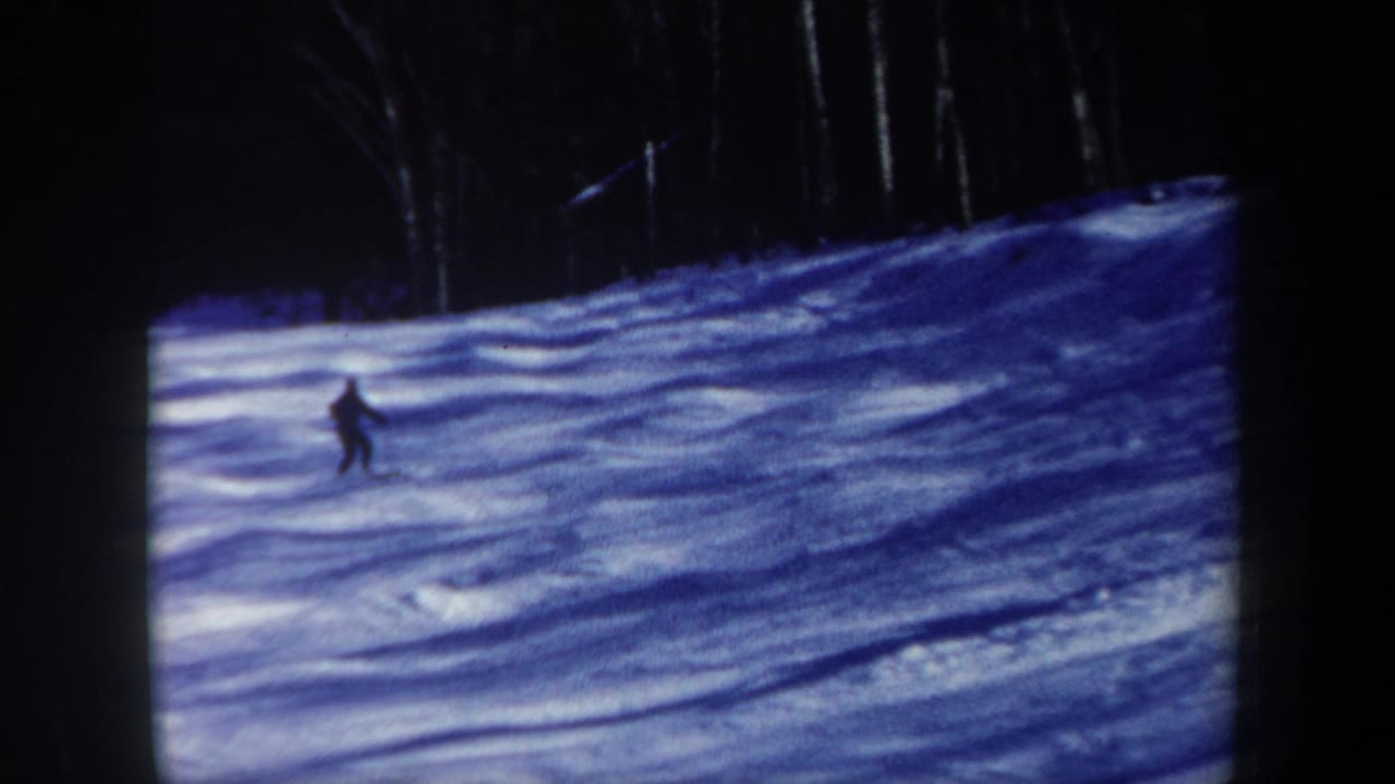 1962 New Hampshire 8mm frame with a distant lone skier descending a blue-shadowed snowy run beside dark trees.