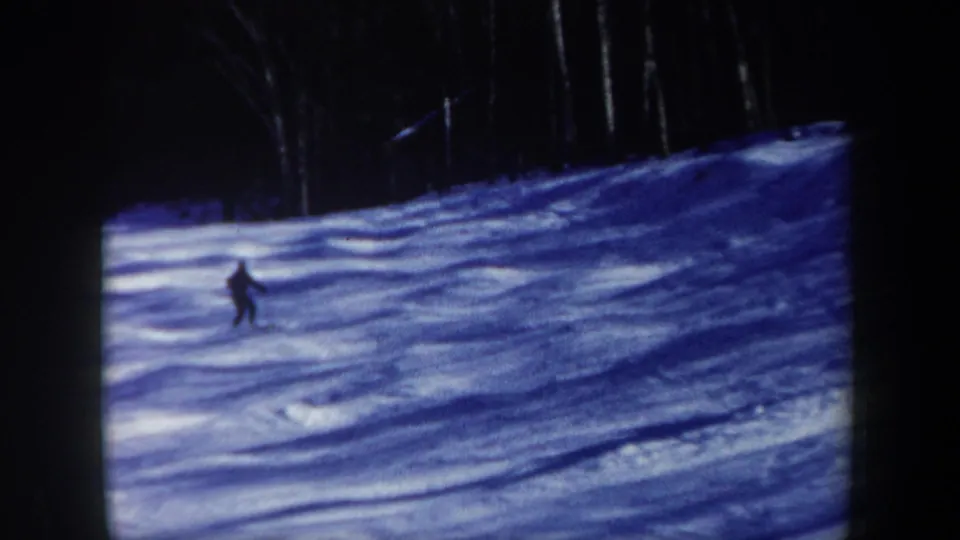 1962 New Hampshire 8mm frame with a distant lone skier descending a blue-shadowed snowy run beside dark trees.