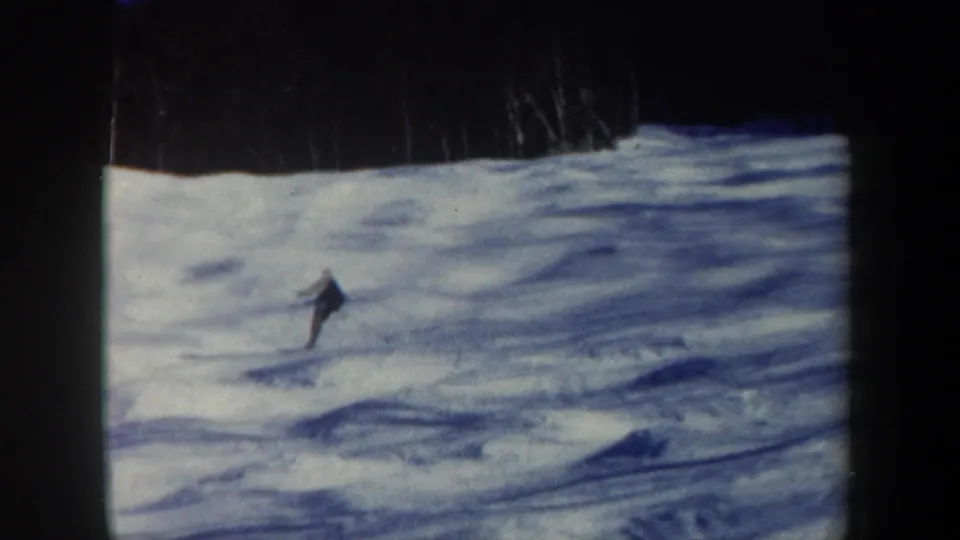 A lone skier leans into the descent on a grainy blue-cast 8mm view of a New Hampshire ski slope.