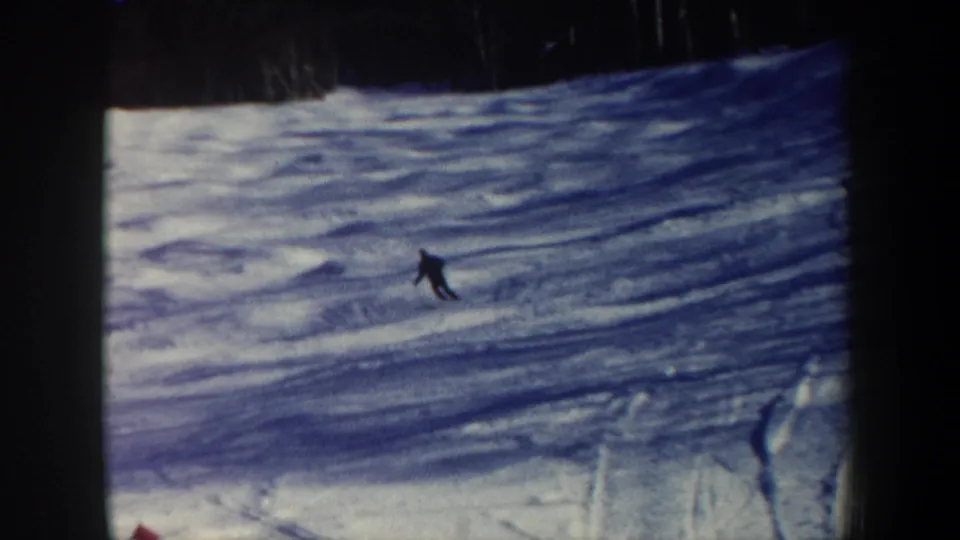 The skier recedes on a wide snowy New Hampshire slope, with the home-movie frame emphasizing open snow and dark treeline.