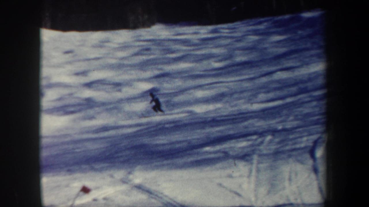 1962 New Hampshire 8mm frame showing a distant lone skier on a wide snow-covered slope with tree shadows and dark film borders.