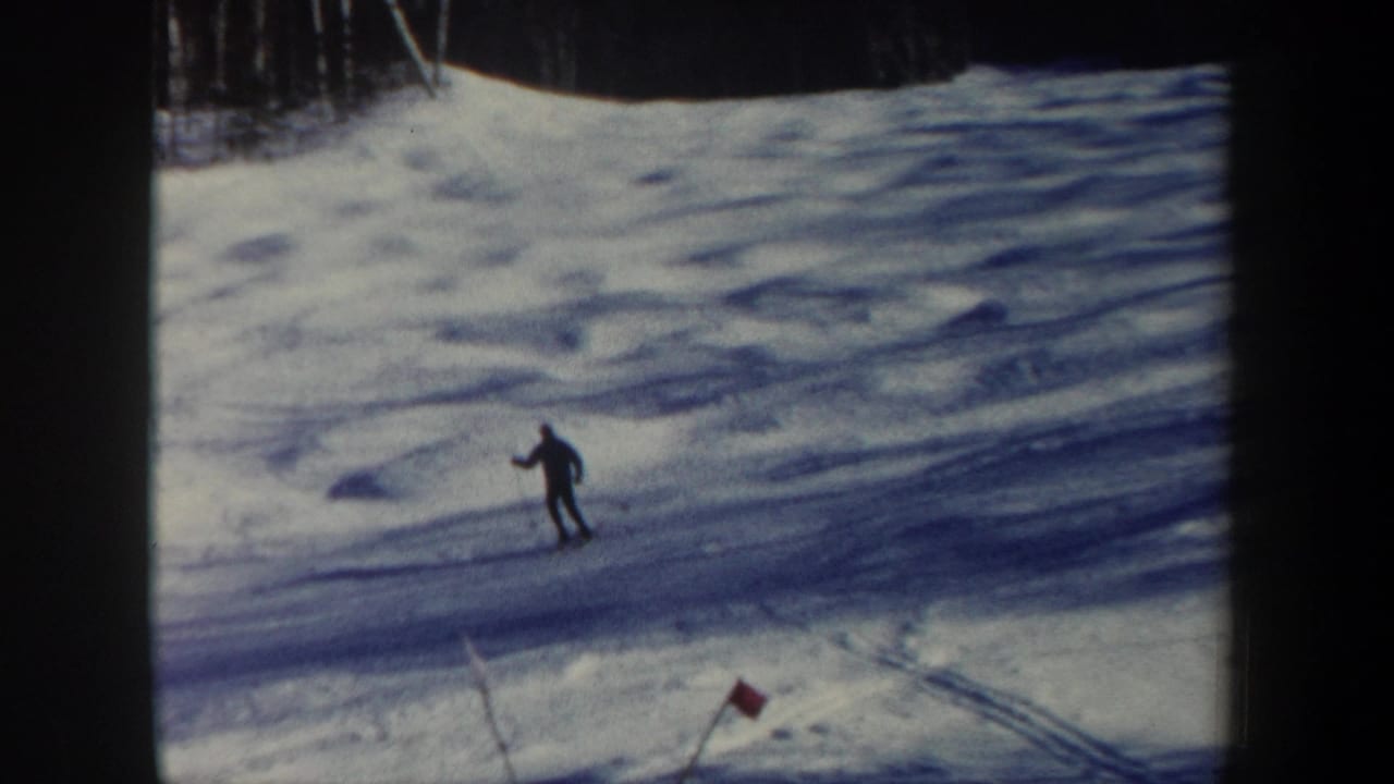 Distant skier descending a snowy hill near a red slope marker.
