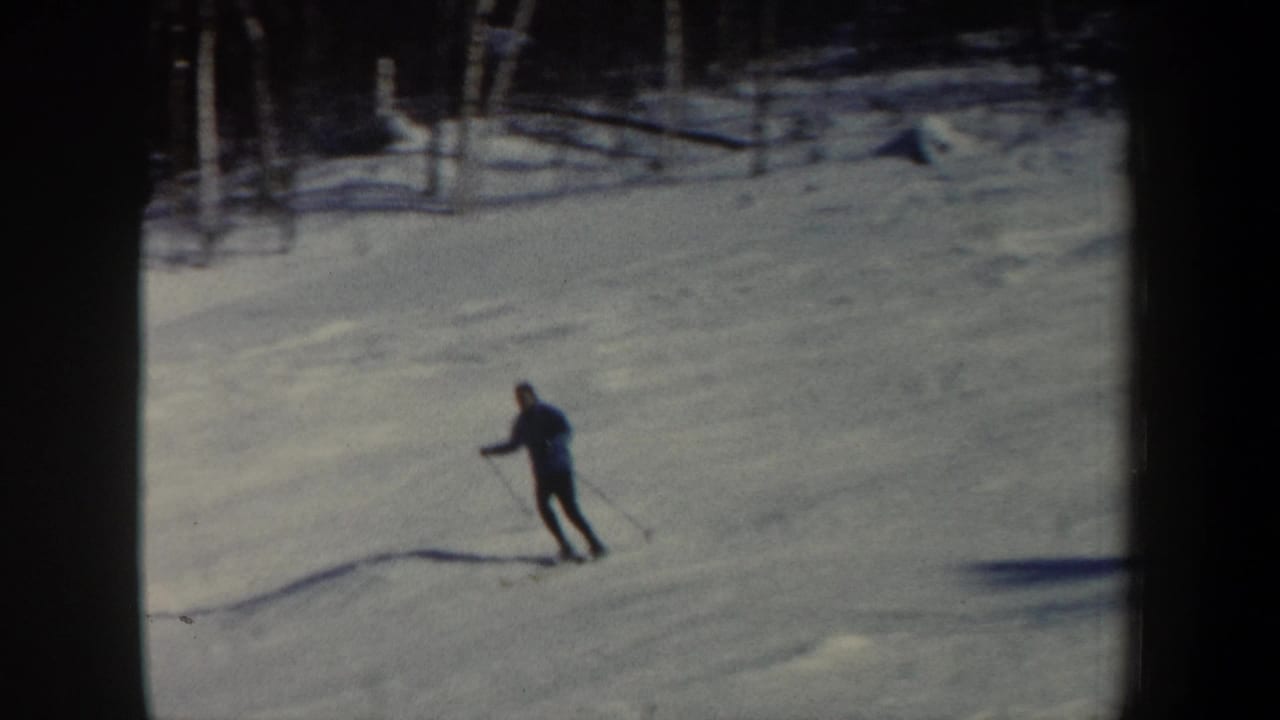 A distant man skis across a snowy wooded slope in 1962 New Hampshire home-movie footage.