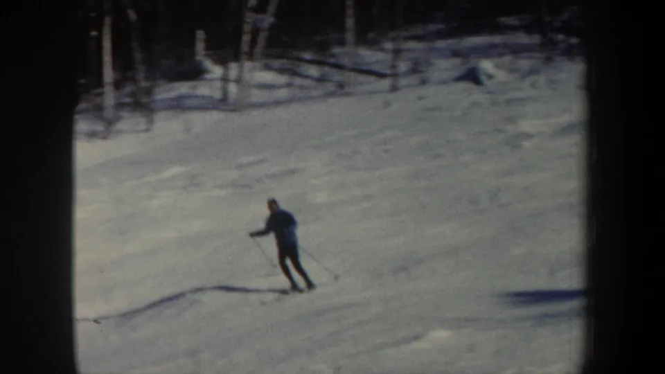 A distant man skis across a snowy wooded slope in 1962 New Hampshire home-movie footage.