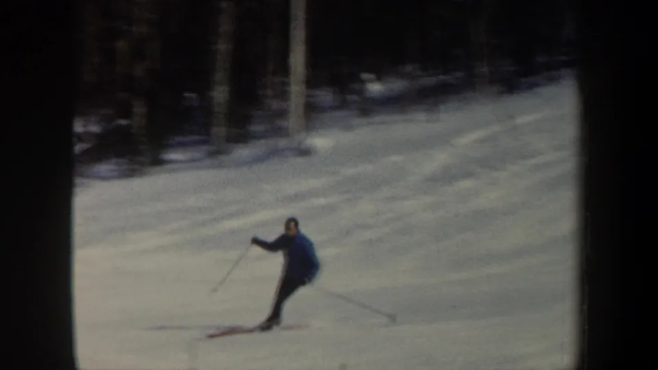 A man in a blue winter jacket turns on skis on a snowy New Hampshire slope in 1962 footage.
