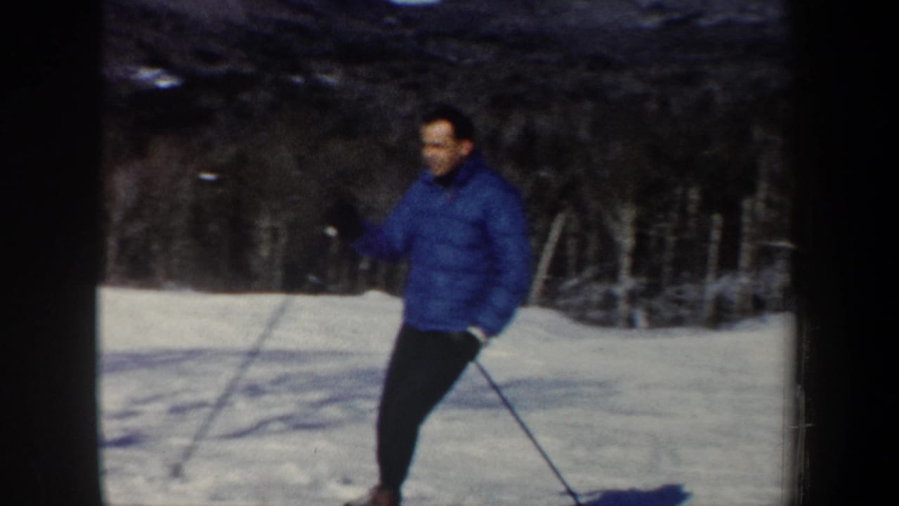 Adult skier in a blue jacket and dark pants moves across a snowy New Hampshire slope in 1962 home-movie footage.
