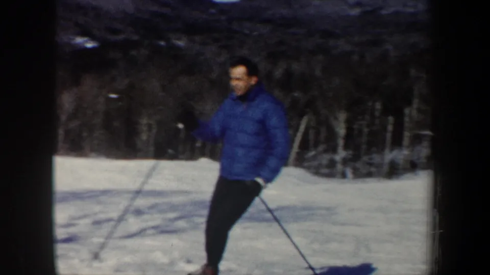 Adult skier in a blue jacket and dark pants moves across a snowy New Hampshire slope in 1962 home-movie footage.
