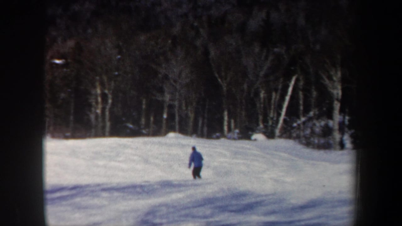 Small figure in a blue jacket skiing downhill on an open snowy slope.