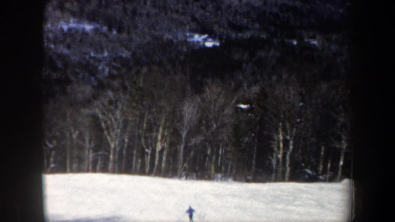 Distant skier on a New Hampshire snowfield in a 1962 8mm frame, with leafless woods and dark hillside beyond.