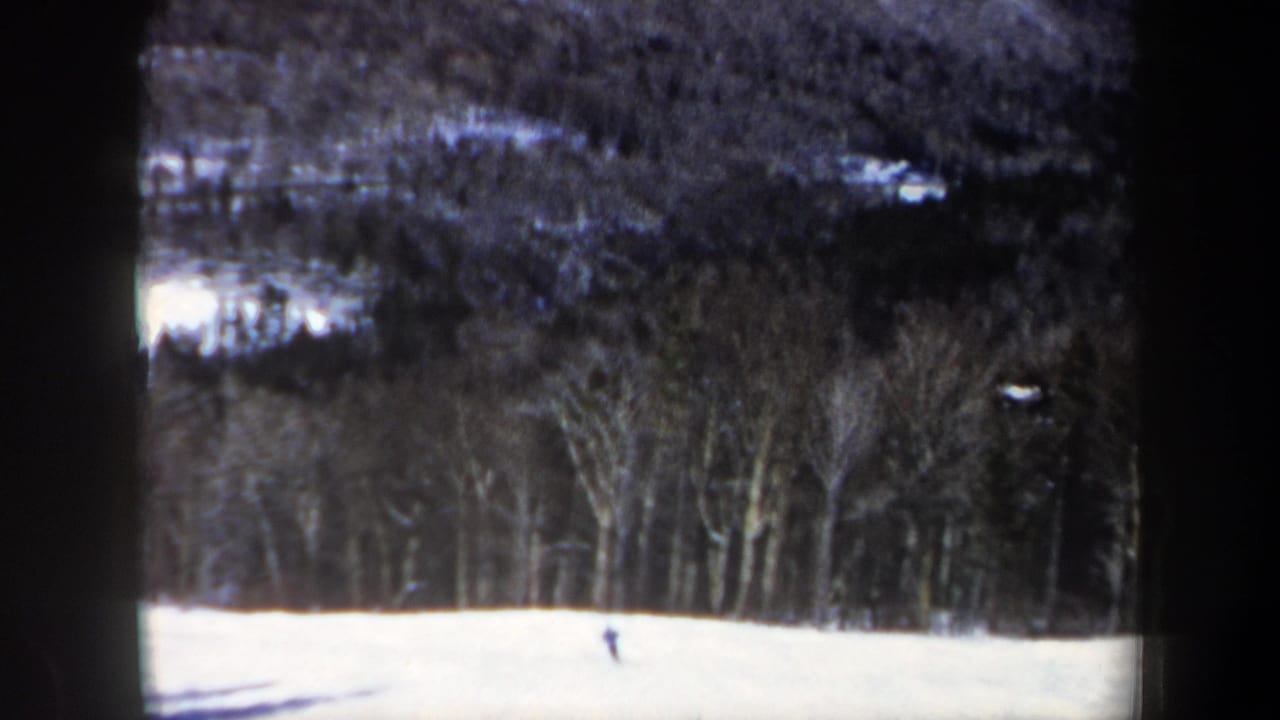 Final 1962 New Hampshire frame showing the skier farther across the snowy slope, with dense bare trees in the background.
