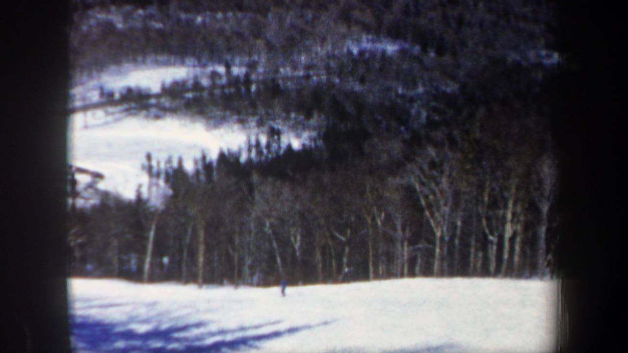Small skier on a bright snow slope with trees and hills in the background.