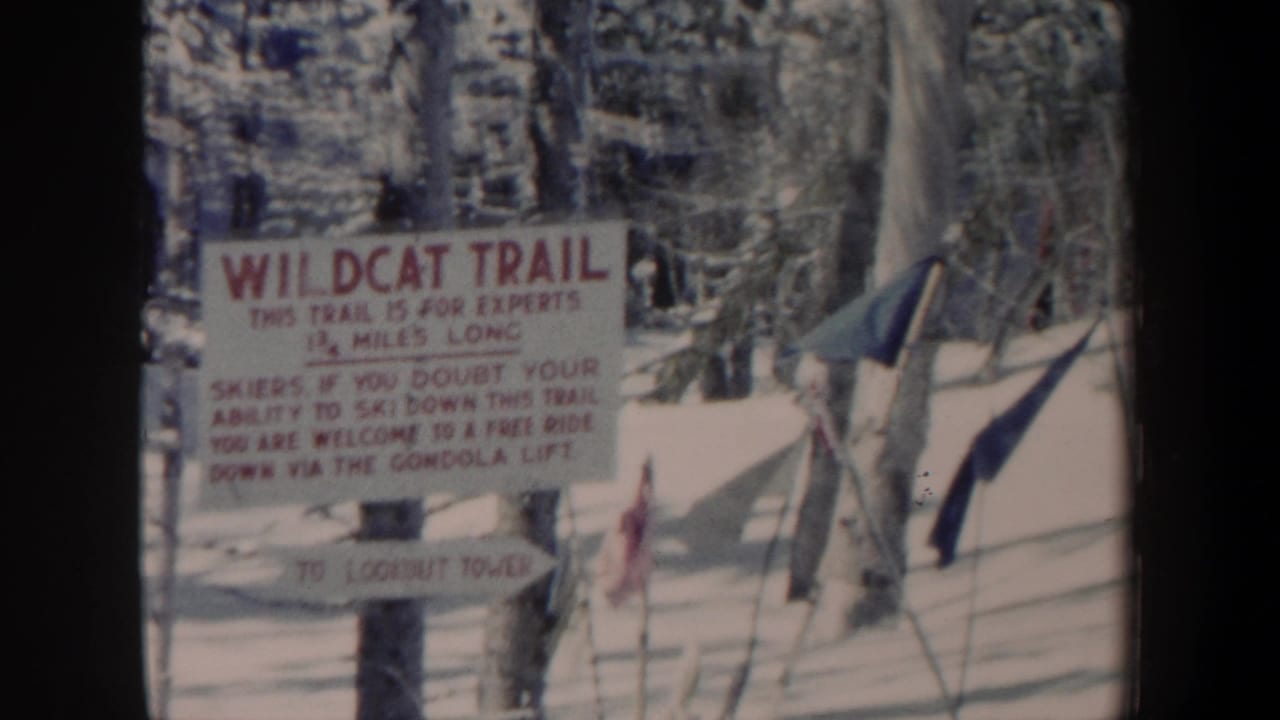 1962 New Hampshire 8mm frame showing a Wildcat Trail sign in snow, with trees, ski poles, and a small flag nearby.