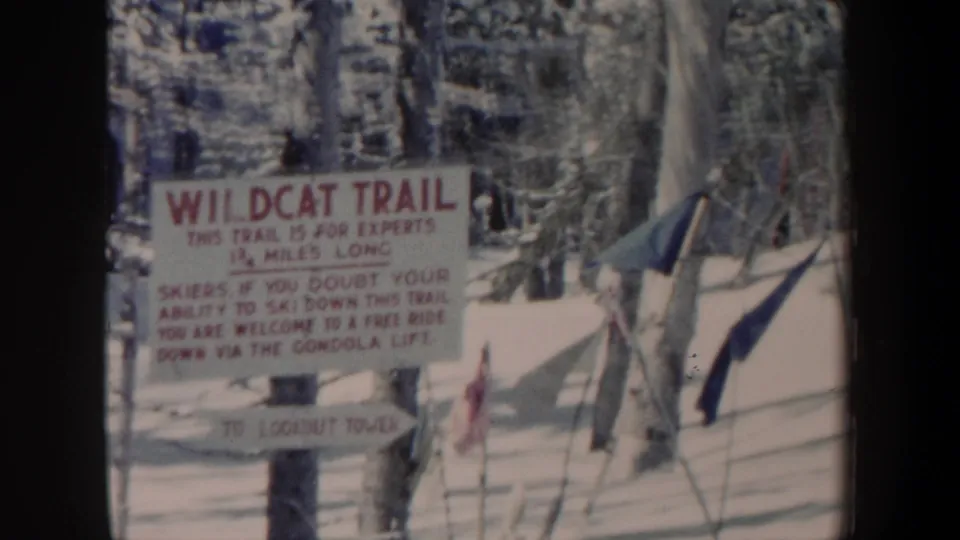 1962 New Hampshire 8mm frame showing a Wildcat Trail sign in snow, with trees, ski poles, and a small flag nearby.