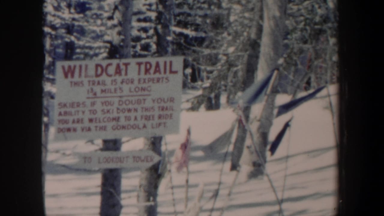 Faded 8mm frame from 1962 New Hampshire showing the Wildcat Trail sign, snowy ground, trees, and nearby ski poles.