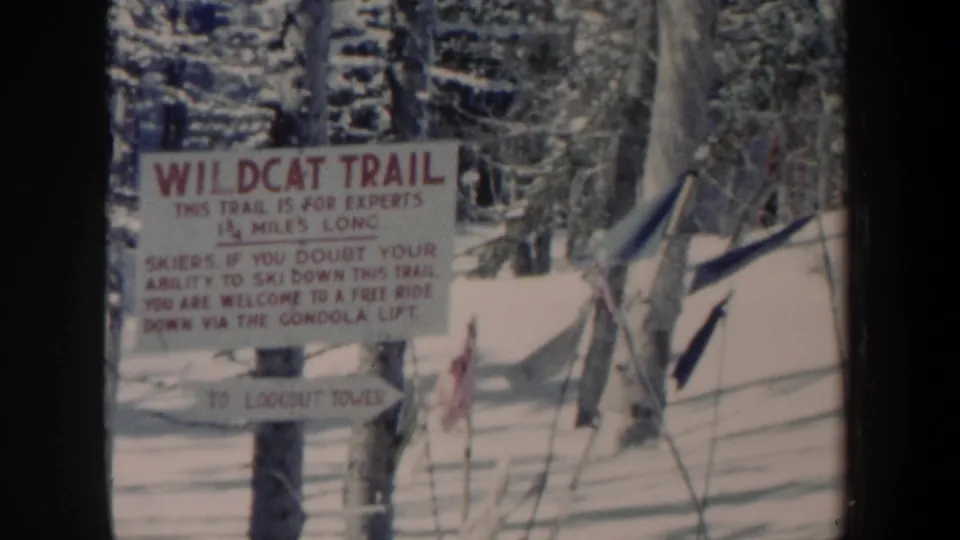 Faded 8mm frame from 1962 New Hampshire showing the Wildcat Trail sign, snowy ground, trees, and nearby ski poles.