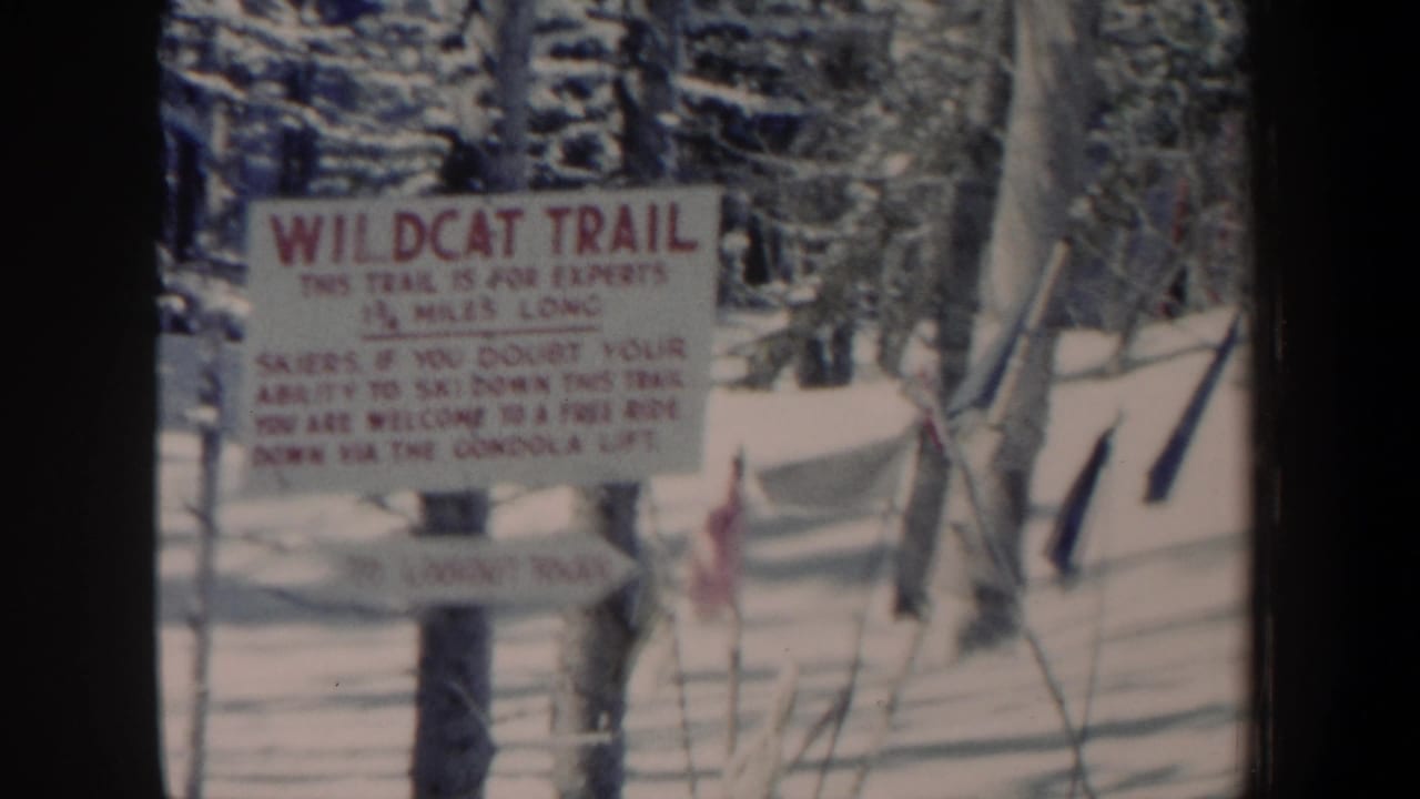 1962 New Hampshire 8mm still of a Wildcat Trail warning sign amid snow, bare trees, ski poles, and a small red flag.