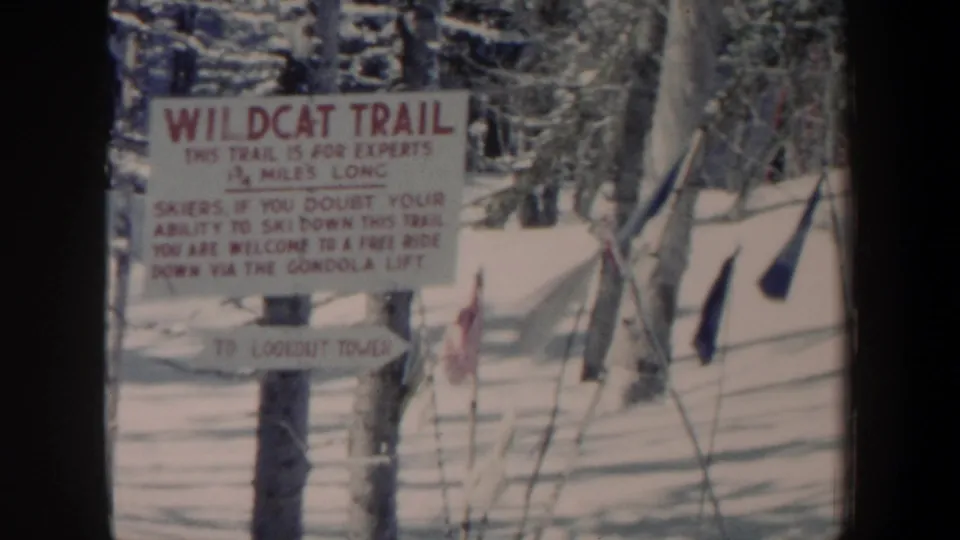 1962 New Hampshire 8mm frame showing a Wildcat Trail sign warning skiers on a snowy wooded slope.