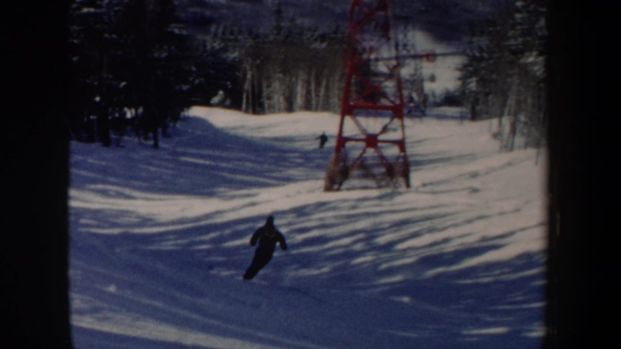 A distant skier moves downhill on a snowy New Hampshire slope near a red lift tower in this 1962 8mm frame.