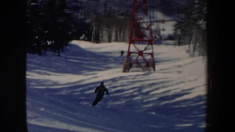 A distant skier moves downhill on a snowy New Hampshire slope near a red lift tower in this 1962 8mm frame.