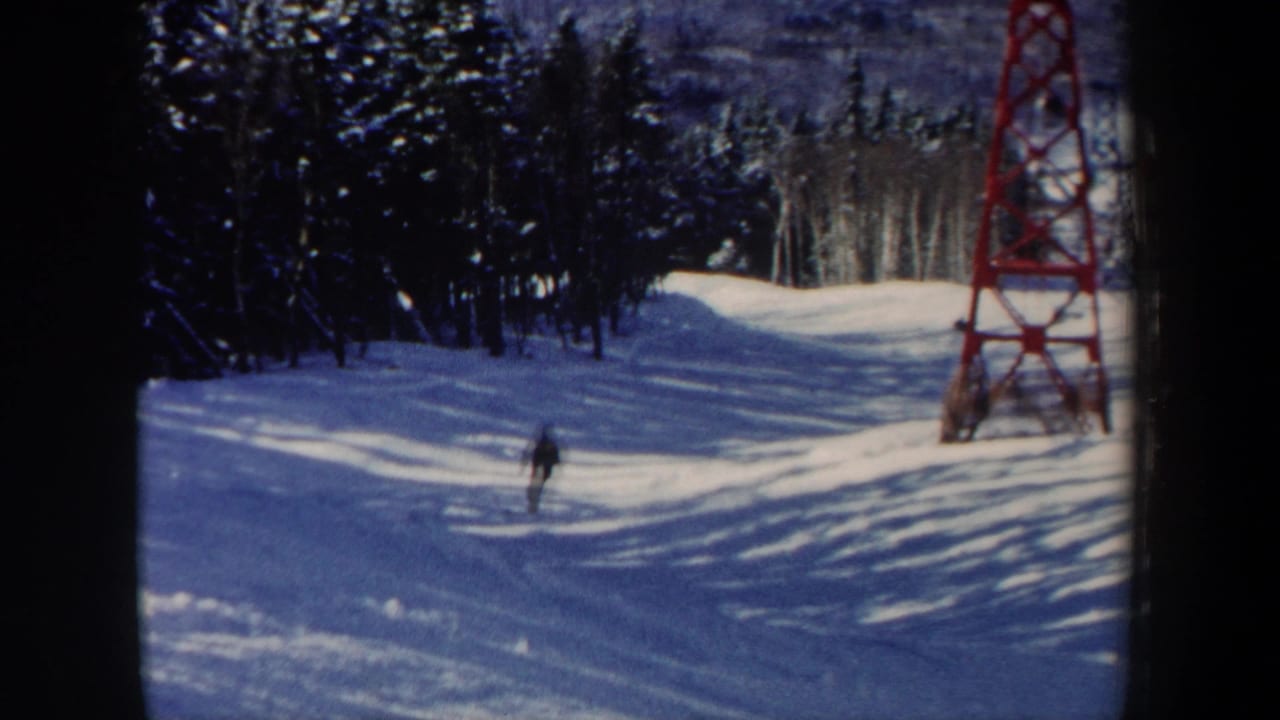 Distant skier on a snowy slope near a red ski lift tower and evergreen trees.