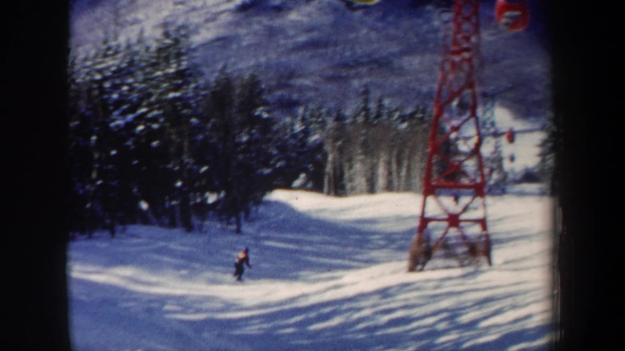 1962 New Hampshire ski-area frame with a skier on a gentle slope, evergreen trees, a red lift tower, and a small cable car overhead.